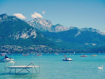 People boating in lake annecy against mountains on sunny day