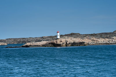 Lighthouse on sea by buildings against clear blue sky