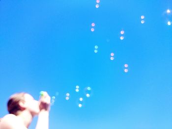 Low angle view of woman jumping against clear blue sky