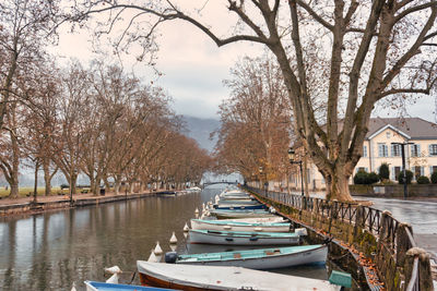 Boats moored on canal amidst trees and buildings against cloudy sky