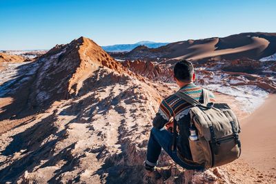 Rear view of man sitting on mountain against clear sky