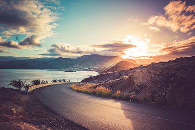 Road by sea against sky during sunset