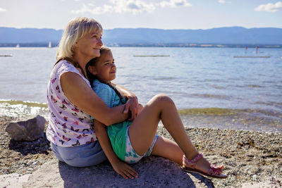 Grandmother and granddaughter sitting on rock at beach