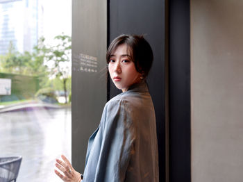 Portrait of young woman standing against window