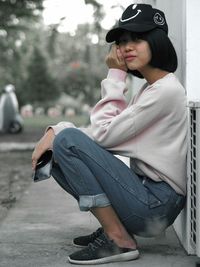 Side view portrait of young woman crouching on footpath