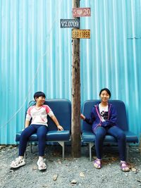 Portrait of sister with brother sitting on chair against wall