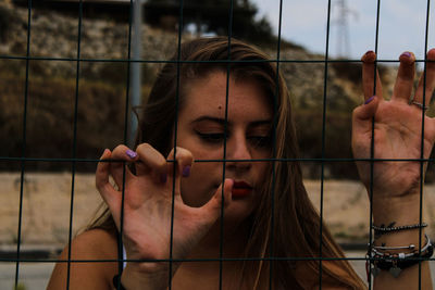 Close-up of woman standing by chainlink fence outdoors