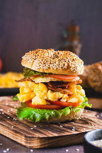 Homemade bagel with scramble egg, bacon, cheese, tomato and lettuce on a board vertical view