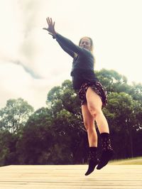 Full length of woman with arms raised against trees