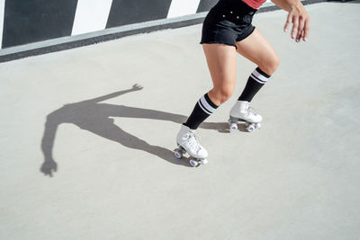 Crop anonymous sportive female roller skater riding on path while doing trick on sunny street during intense training in city