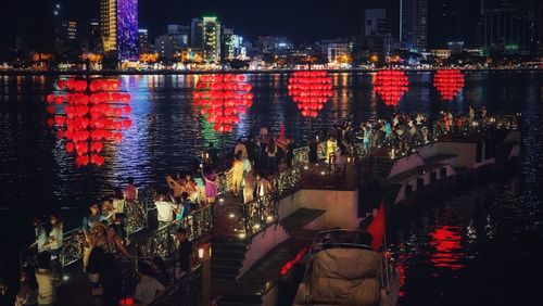 Panoramic view of crowd at illuminated city by river at night