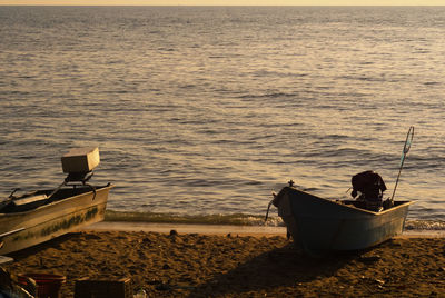 Boat moored on shore against sky during sunset