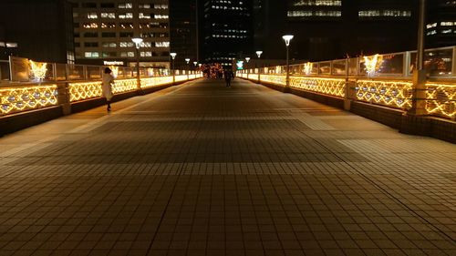 Illuminated footpath amidst buildings in city at night