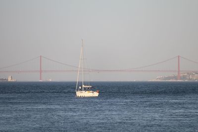 Yacht over tagus river against 25 de abril bridge