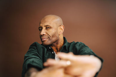 Bald mature man gesturing against brown background