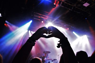 Cropped silhouette hands making heart shape at music concert