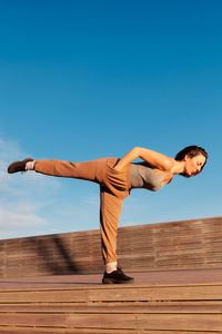 Full body side view of sportive female in activewear practicing single leg deadlift during outdoor training on street of city