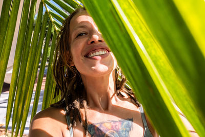 Smiling woman taking selfie under palm leaf on tropical beach. summery vacations moment.