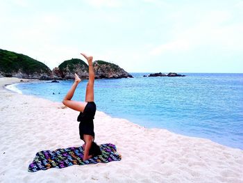 Side view of woman practicing headstand at beach