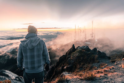 Rear view of man standing on mountain against sky during sunset