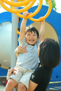 Mother assisting son in climbing jungle gym standing on playground