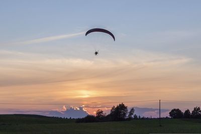 Silhouette person paragliding against sky during sunset