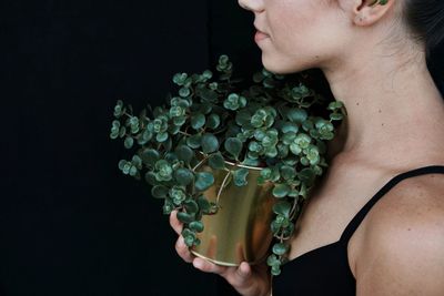 Midsection of woman holding potted plant against black background