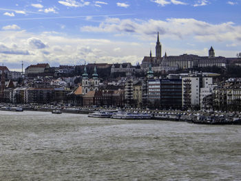 Buildings at waterfront against cloudy sky