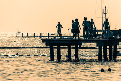 Silhouette people standing by sea against clear sky during sunset