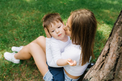 Young caucasian mother kisses her three-year-old son on the cheek while sitting in the park