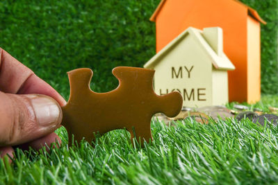 Cropped hand holding jigsaw piece against model house on field