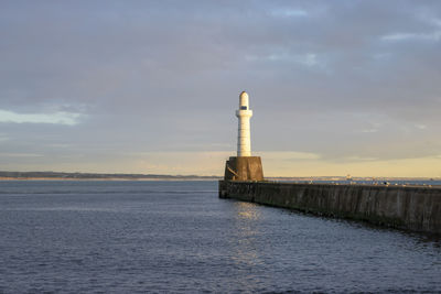 Lighthouse by sea against sky during sunset