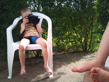 Full length of young woman using mobile phone while sitting on tree