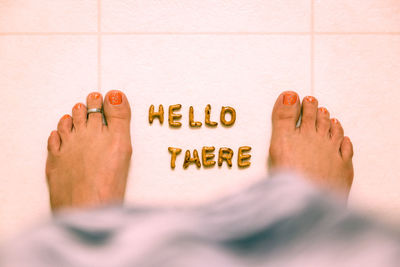 Low section of woman with hello there text on tiled floor