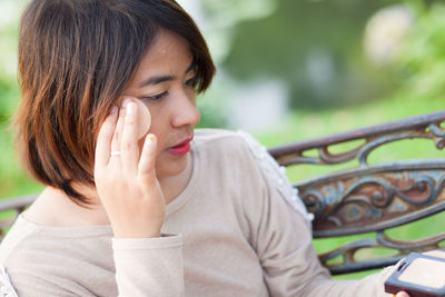 Close-up of young woman applying foundation while sitting on bench