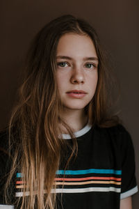 Charming teen girl with long hair looking at camera on dark background in studio