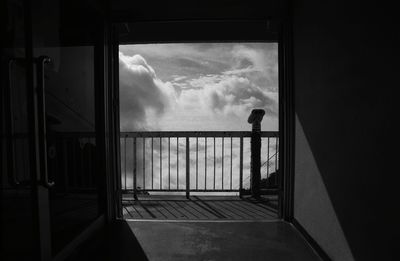 Silhouette man standing by window against sky