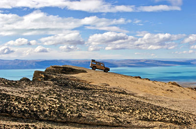 Vehicle on mountain by sea against sky