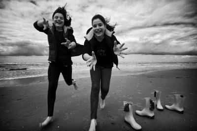Playful friends running at beach against sky
