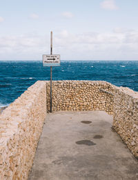 Sign board on pier by sea against sky