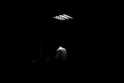 Rear view of man sitting in illuminated darkroom