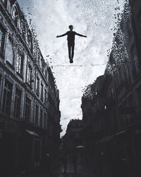 Digital composite of man jumping amidst buildings against sky at dusk