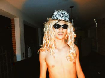 Portrait of shirtless man wearing wig and sunglasses at home