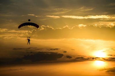 Silhouette person paragliding against sky during sunset