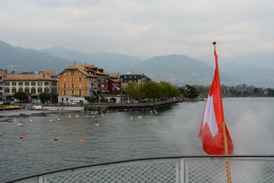 Red flag on river by buildings against sky