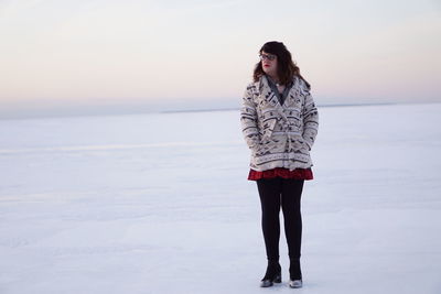 Transgender male standing on snowfield against sky during sunset