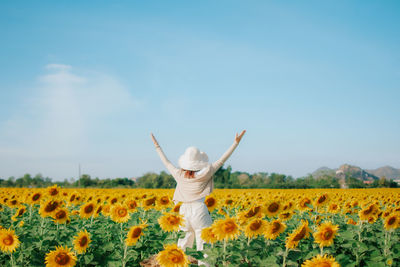 Rear view of woman with arms raised standing on field against sky