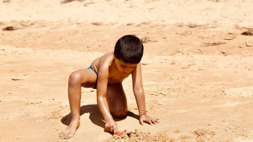 Full length of shirtless boy playing with sand at beach