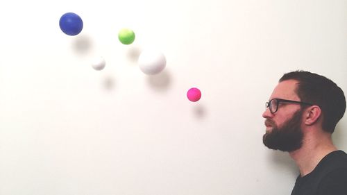 Side view of man looking at multi colored balls against wall