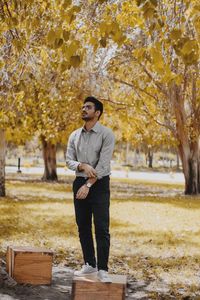 Young man looking away while standing by tree during autumn